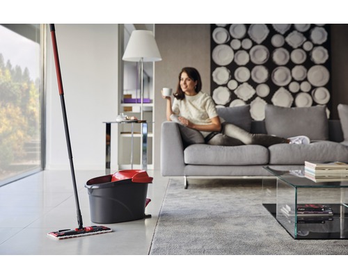 Mop cu găleată într-o cameră de zi luminoasă, femeie relaxându-se pe canapea