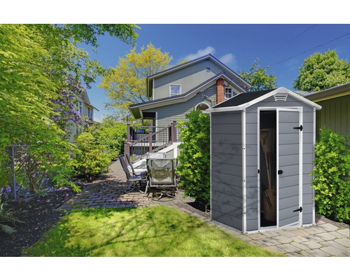 Scenă de grădină cu magazie de scule în fața unei case cu terasă și mobilier de grădină.