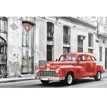 Mașină de epocă roșie în fața unei clădiri cu steag cubanez