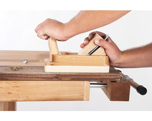 O persoană rindeluiește o piesă de lucru cu un rindel dublu pe un banc de lucru.