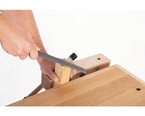 Artizan prelucrează o bucată de lemn cu o rașpă de lemn pe un banc de lucru