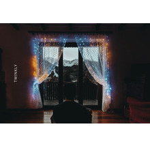 Persoană în fața ferestrei cu perdea luminoasă Twinkly și vedere la munte