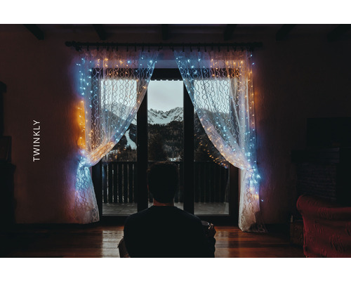 Persoană în fața ferestrei cu perdea luminoasă Twinkly și vedere la munte