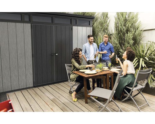 Scenă de grădină cu o magazie de unelte și un grup de oameni care mănâncă și beau împreună.