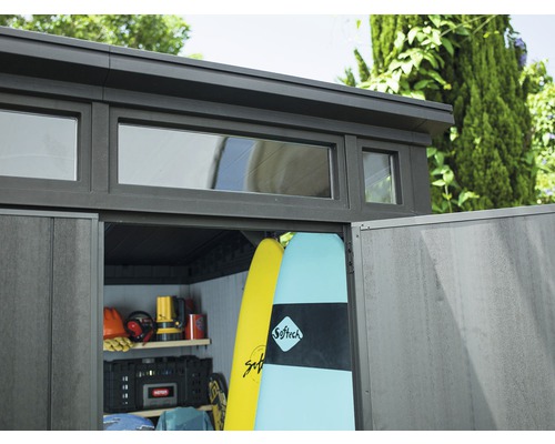 Șopron de grădină cu ferestre și uși deschise, plin cu scânduri de surf și unelte.