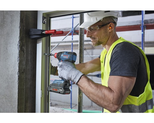 Un meșter folosește o șurubelniță cu impact cu acumulator pe un toc de fereastră pe un șantier de construcții.