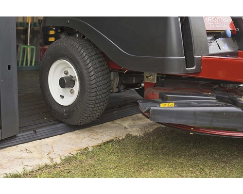 Tractor de gazon pe covor de cauciuc în fața unui garaj