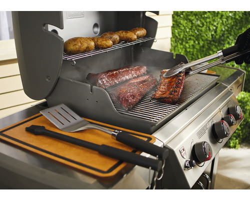 Grătar cu coaste, carne și cartofi pe grătar, clește de grătar și spatulă la îndemână.