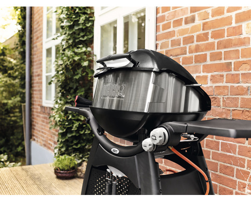 Grătar cu gaz Weber cu capac în fața unui zid de cărămidă roșie