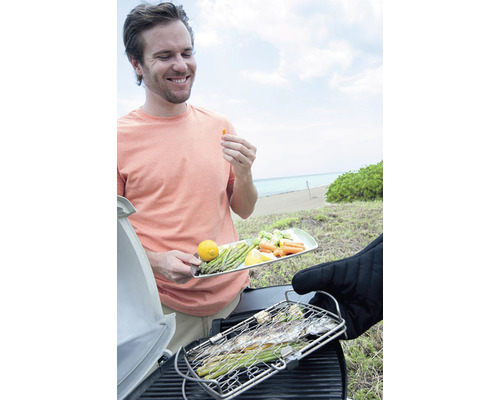 Bărbat care face grătar cu pește și legume pe plajă.