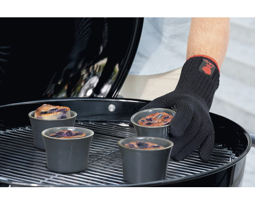 Persoană cu mănușă de grătar așezând forme de gratin cu prăjitură cu afine pe un grătar.