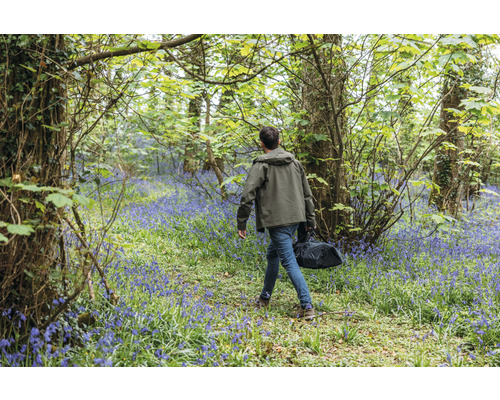 Bărbat cu geantă mergând printr-o pădure cu zambile înflorite