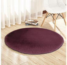 Covor rotund cu fibre lungi pe podea de lemn, cu un scaun și cărți în fundal.