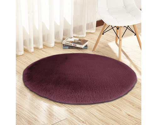 Covor rotund cu fibre lungi pe podea de lemn, cu un scaun și cărți în fundal.