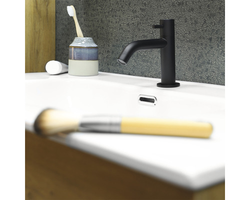 Baterie de lavoar neagră pe o chiuvetă albă cu periuță de dinți, pastă de dinți și pensulă de machiaj