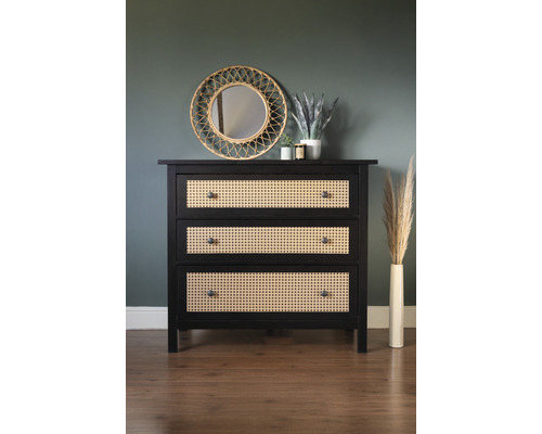 Comodă cu trei sertare din lemn și împletitură de ratan în fața unui perete cu oglindă și decorațiuni.