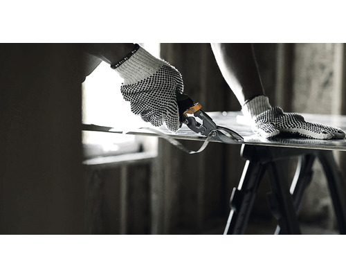 O persoană cu mănuși de lucru taie tablă cu foarfece de tablă pe o masă de lucru.