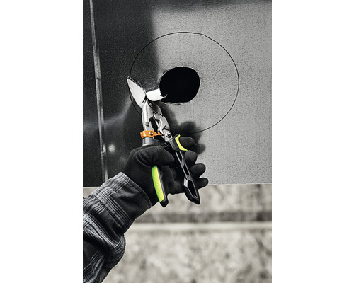 O persoană taie o gaură într-o tablă metalică cu o foarfecă de tablă.