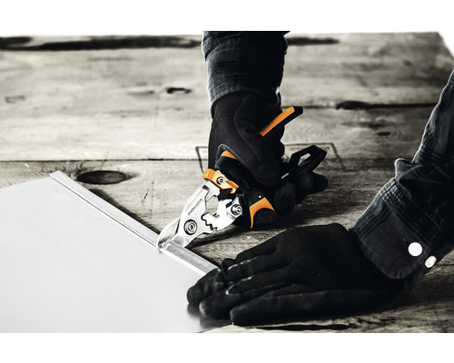 O persoană taie o foaie de metal cu o foarfecă de tablă.