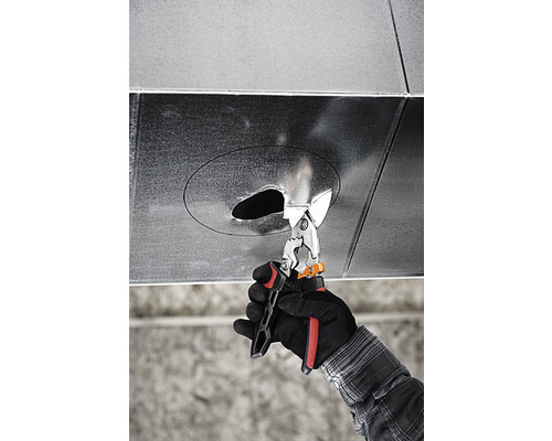 O mână cu mănușă taie o gaură într-un tub de ventilație cu foarfece de tablă.