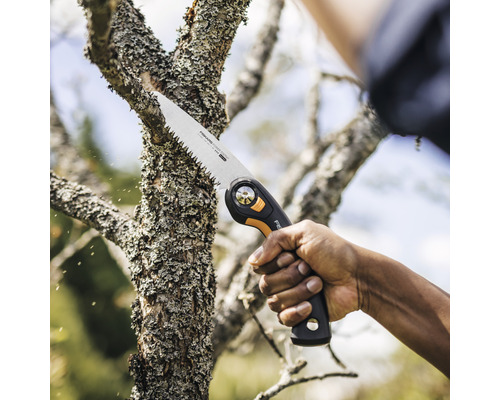 O persoană taie o ramură de copac cu un fierăstrău de grădină.