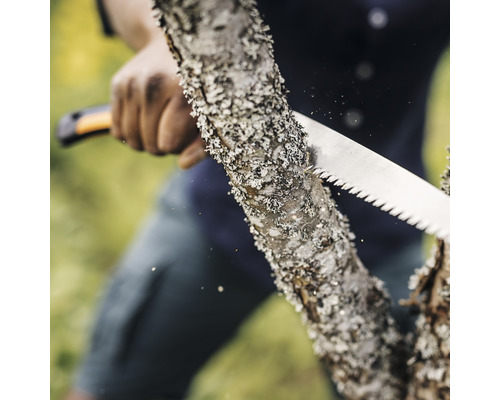 O persoană taie un trunchi de copac cu un ferăstrău manual.
