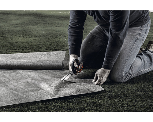 O persoană taie pânză anti-buruieni cu foarfeca pe un gazon.