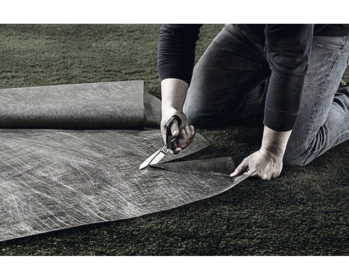 O persoană taie folie anti-buruieni cu foarfeca pe gazon.