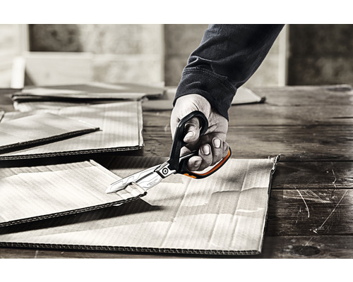 O mână taie carton cu o foarfecă.