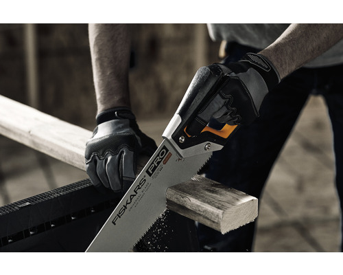 O persoană taie o scândură de lemn cu un ferăstrău manual marca Fiskars.