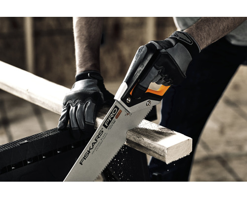 O persoană taie o bucată de lemn cu un fierăstrău manual. Persoana poartă mănuși de lucru. Logo Fiskars.