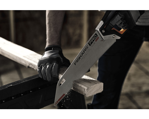 O persoană taie cu un ferăstrău manual o bucată de lemn pe un suport de tăiere.