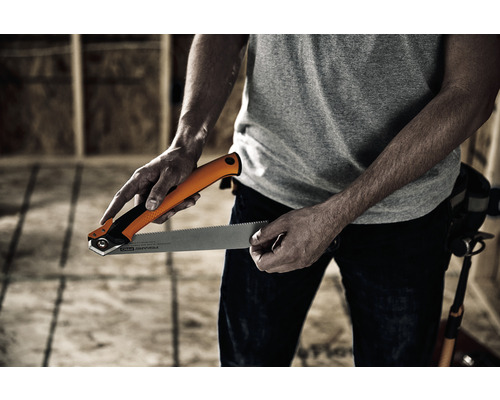 O persoană ține un fierăstrău manual în fața unui perete în construcție brută.