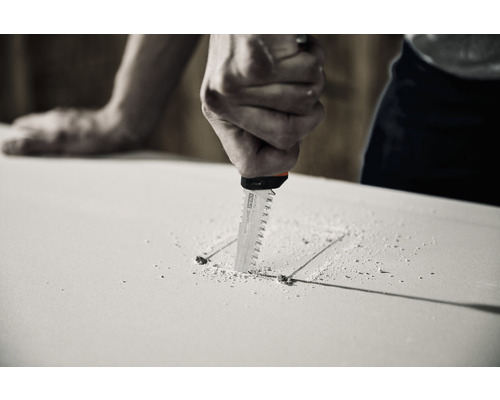 Un meșter taie o gaură dreptunghiulară într-o placă de gips-carton cu un ferăstrău de traforaj.