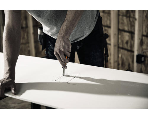 Un bărbat taie o gaură într-o placă de gips-carton cu un fierăstrău pentru gips-carton.