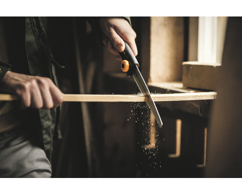 Un fierăstrău manual taie o scândură de lemn.