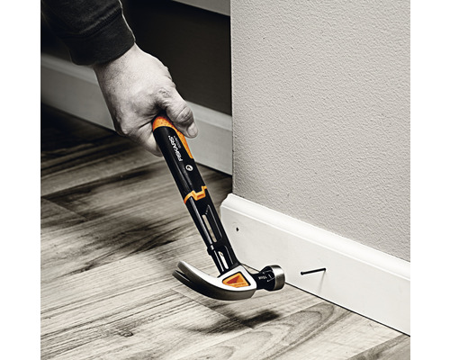 O persoană bate un cui într-o plintă cu un ciocan Fiskars.