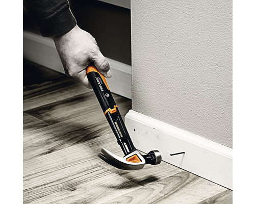 Un bărbat bate un cui într-o plintă cu un ciocan.