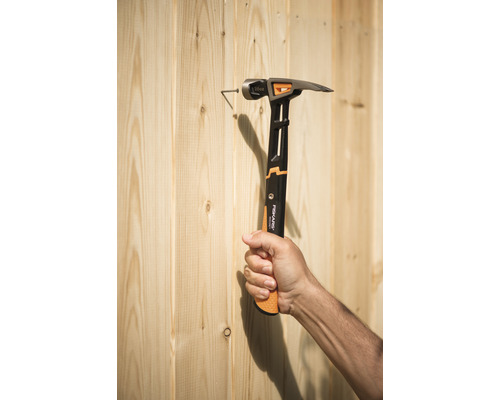 Mână ținând un ciocan bătând un cui într-un perete de lemn