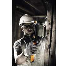 Un muncitor în construcții cu cască de protecție și mănuși bate un cui cu un ciocan într-o bucată de lemn.