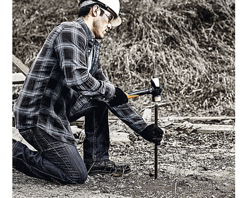 Un bărbat bate un par de împământare în pământ cu un ciocan.