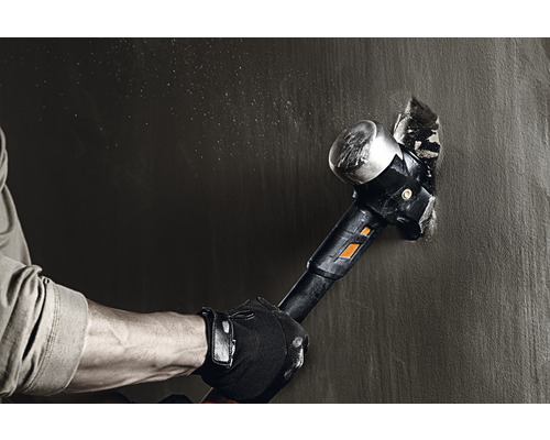 Un bărbat lovește un zid cu un ciocan mare.