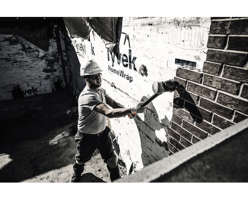 Un muncitor în construcții cu un ciocan mare care efectuează lucrări de demolare pe un zid de cărămidă