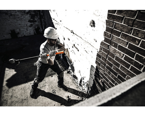 Un muncitor în construcții cu cască de protecție lucrează la un zid de cărămidă cu o rangă.