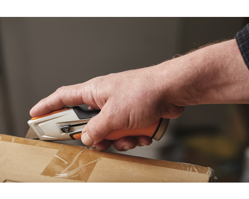 Mână care deschide un pachet cu un cuțit pentru covoare