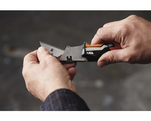 Mâini care țin un cuțit Fiskars cu o lamă extinsă