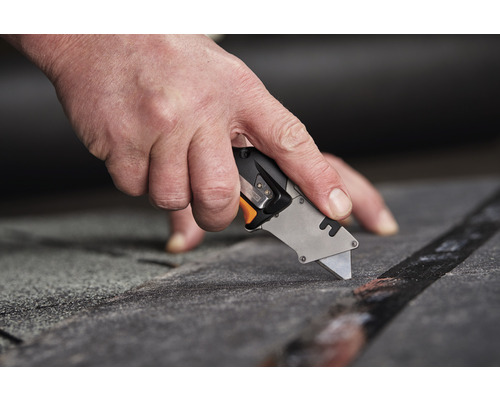 O mână taie un material cu un cuțit universal.