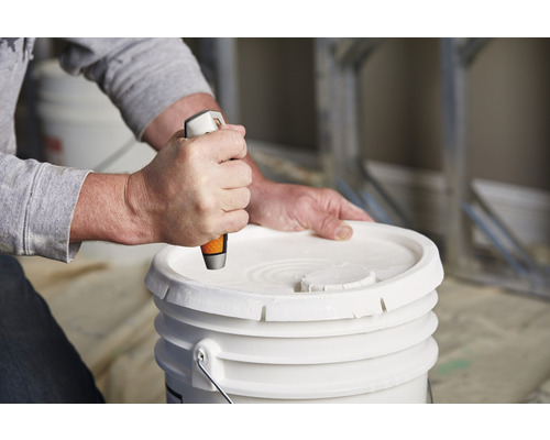 O persoană deschide o găleată cu vopsea cu o unealtă.