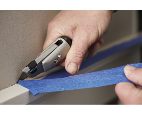 O persoană taie bandă de mascare pe un perete cu un cutter.