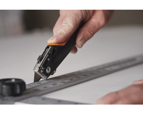 O mână taie cu un cuțit de-a lungul unei rigle metalice pe o suprafață.